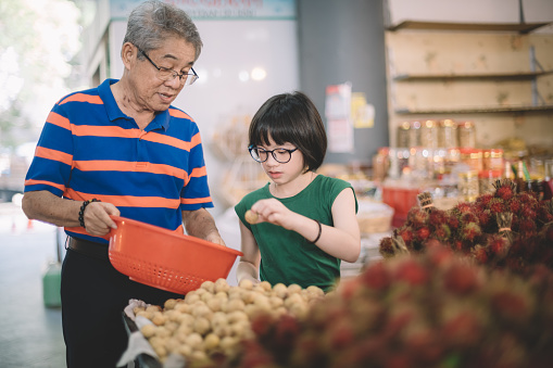 an asian chinese grandfather is selecting lanzone (duku langsat)  at the fruit stall with his grandchild