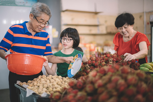 an asian chinese grandparents are selecting lanzone (duku langsat) and rambutan at the fruit stall with their grandchild