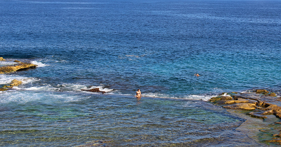 Sliema, Malta - 6th November 2018: People swimming and relaxing at Fond Ghadir rocky beach with natural pool in Sliema