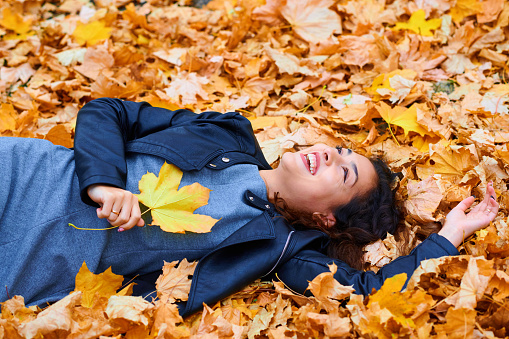 woman lying with autumn leaves in city park, outdoor portrait