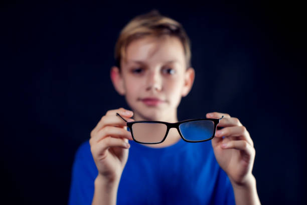 A portrait of a boy holds eyeglasses in hands in front of dark background. Children and healthcare concept A portrait of a teen boy holds eyeglasses in hands in front of dark background. Children, ophthalmology and healthcare concept myopia photos stock pictures, royalty-free photos & images