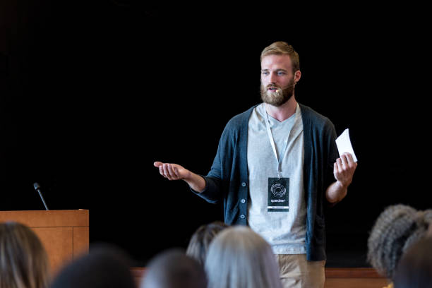 Gesturing to make point, mid adult hipster speaks to audience As he gestures to emphasize his point, the mid adult male hipster speaks to the expo audience during one of the break out sessions. summit meeting stock pictures, royalty-free photos & images