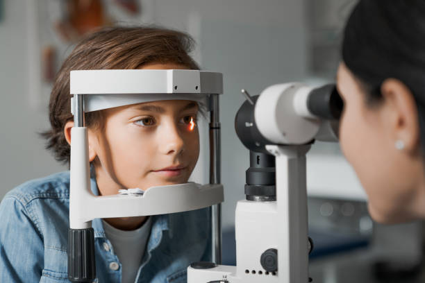 Adult female doctor ophthalmologist is checking the eye vision of cute child in modern clinic stock photo