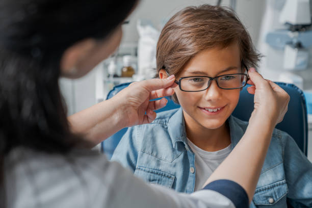 female caucasian doctor putting glasses on little boy in clinic - patient happiness cheerful optometrist imagens e fotografias de stock