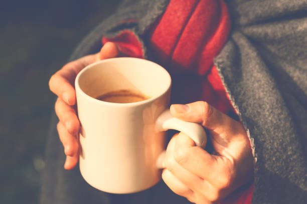 una ragazza fuori casa avvolta in una coperta di lana e con in mano una tazza beige di caffè fresco, illuminata dalla luce del sole - 4598 foto e immagini stock