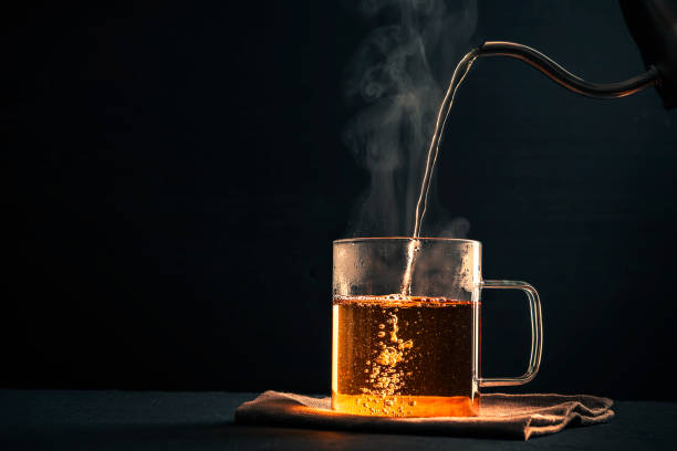 le processus de brassage du thé, verser l'eau chaude de la bouilloire dans la tasse, la vapeur sortant de la tasse, gouttelettes d'eau sur le verre, fond noir - bursting the bubble photos et images de collection