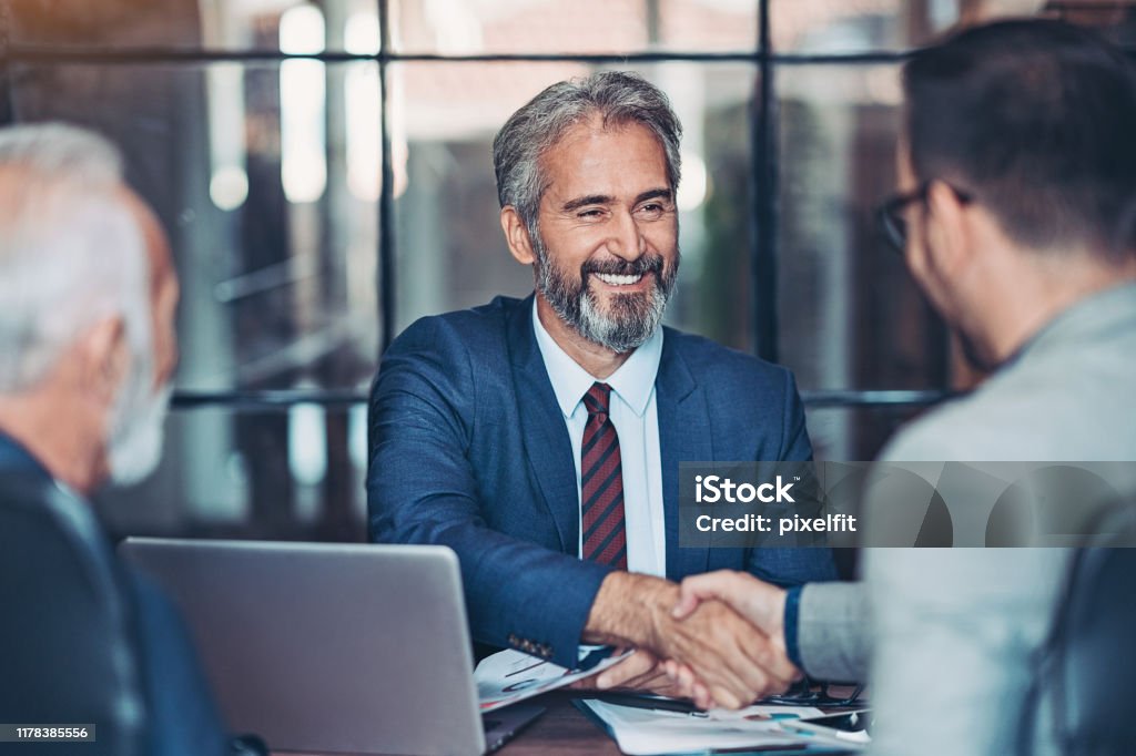 Businessmen handshake in the office Mature businessman shake hands with a younger colleague Business Stock Photo