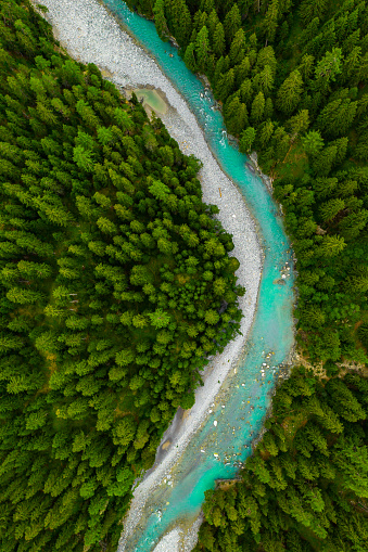 Inn River flowing in the forest in Switzerland. Aerial view from drone on a blue river in the mountains.
