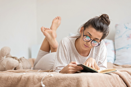 Young beautiful woman reading book in bed