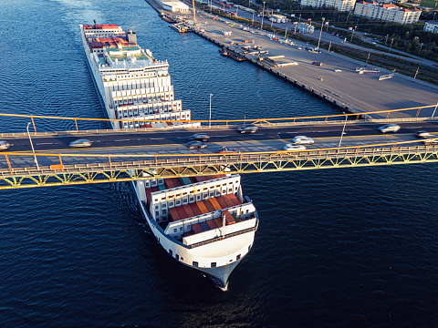 Aerial drone view of a container ship nearing port with the assistance of a tugboat.