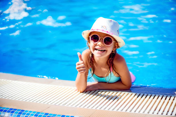 szczęśliwa dziewczyna w okularach przeciwsłonecznych i kapeluszu z jednorożcem pokazuje kciuk w odkrytym basenie luksusowego kurortu na wakacjach na tropikalnej wyspie plażowej - inflatable ring obrazy zdjęcia i obrazy z banku zdjęć