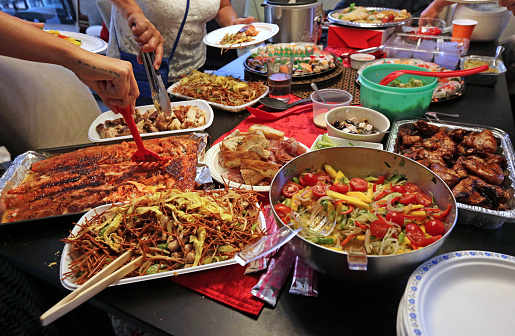 Ottawa, Canada - August 24, 2019: Many dishes include baked salmon, salad, barbecued duck, chow mein, feta cheese and sushi at a dinner party.