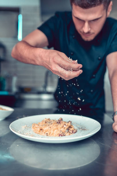 갈은 치즈를 곁들인 남성 시징 파스타 - chef cooking pasta professional occupation 뉴스 사진 이미지