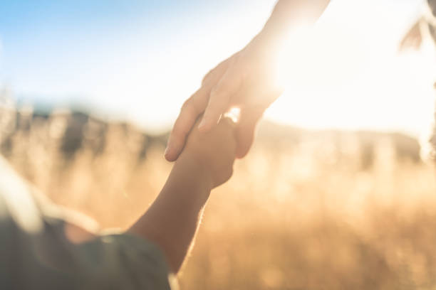 Child holding mothers hand walking outdoors. Mother and her son holding hands while walking in the nature at sunset. kids holding hands stock pictures, royalty-free photos & images