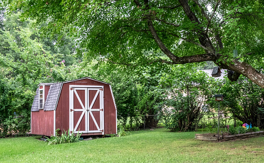 Red barn shed/farmhouse in green wooded area in yard.