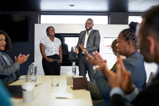 attraente uomo d'affari nero incoraggiato da diversi gruppi multietnici di colleghi durante la presentazione in ufficio - african descent foto e immagini stock