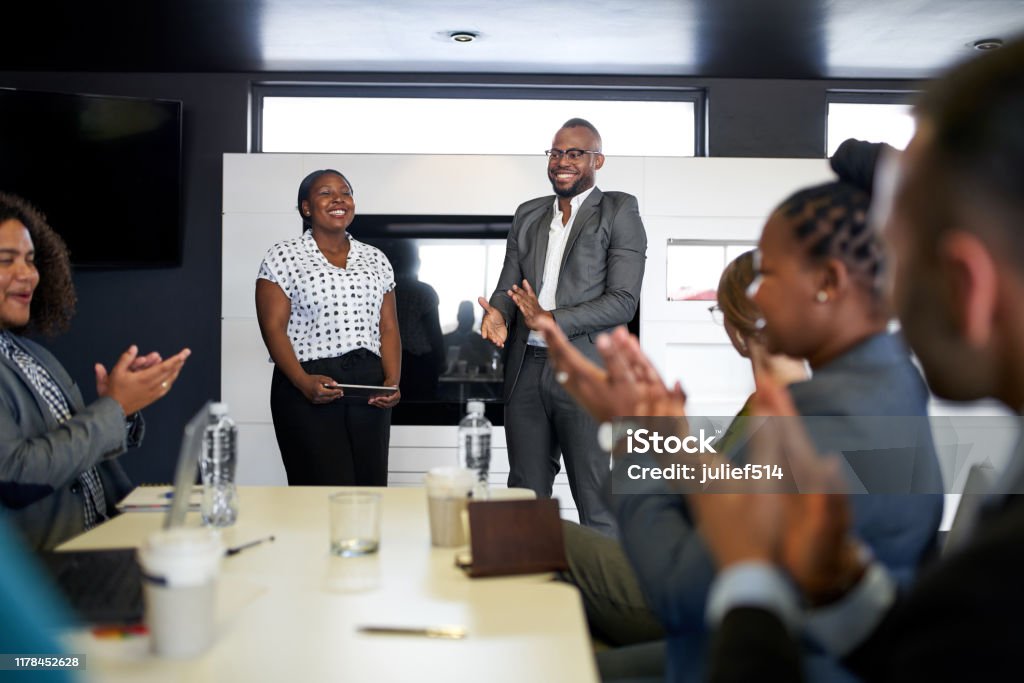 Attractive black businessman being encouraged by diverse multi-ethnic group of coworkers during presentation in office Group of mixed race colleagues in modern meeting room with laptop computer encouraging two attractive African American business professionals leading a collaborative discussion African Ethnicity Stock Photo