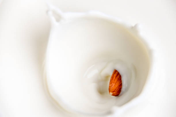 Almond milk splash - with falling almond into a glass of milk - veganism stock photo