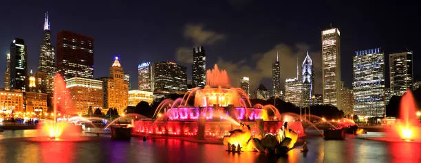 Photo of Chicago skyline illuminated at dusk with colorful Buckingham fountain on the foreground