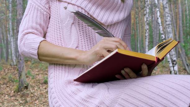 istock Happy attractive smiling woman writes poetry with feather in spring forest. 1178474321