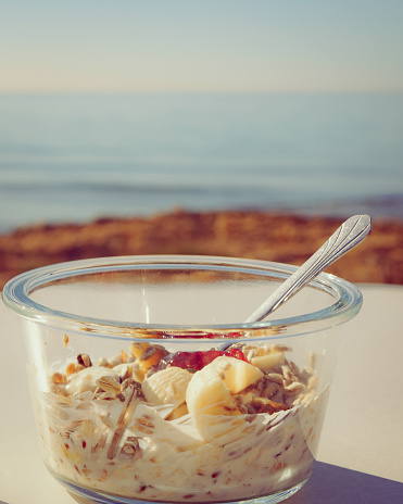 Healthy breakfast on nature. Oatmeal granola with yogurt, banana fruits in bowl, sunny morning, ocean background