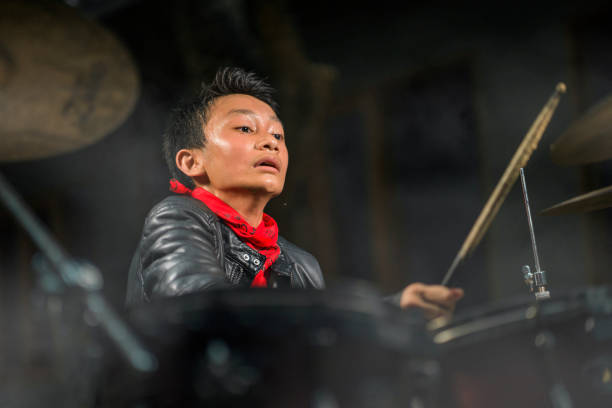 musicien de groupe de rock d'adolescent. 13 ou 14 ans cool et talentueux asiatique américain mixte ethnie garçon jouant de la batterie dans la veste en cuir et bandana pratique et exécutant la chanson - 12 13 years 13 14 years learning education photos et images de collection