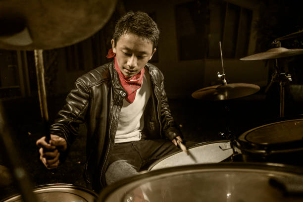 молодой крутой и талантливый музыкант-подросток, играющий на барабанах в возрасте 14 лет в кожаной куртке и стиле рок-группы bandana, практикующ - 13 14 years стоковые фото и изображения