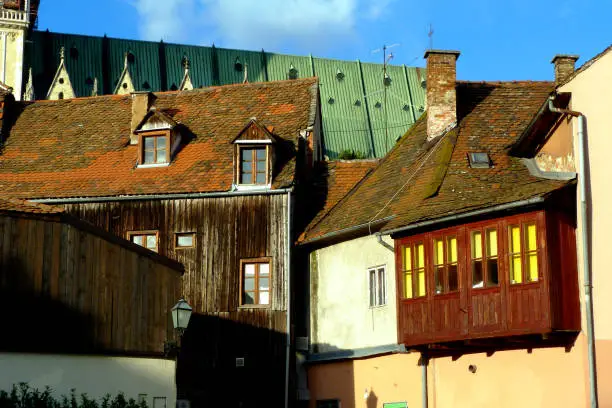 old clay sloped residential roof in downtown Zagreb. small wooden dormers. aged deep brown wood slat finished house exterior with yellow windows. old European architecture & travel concept