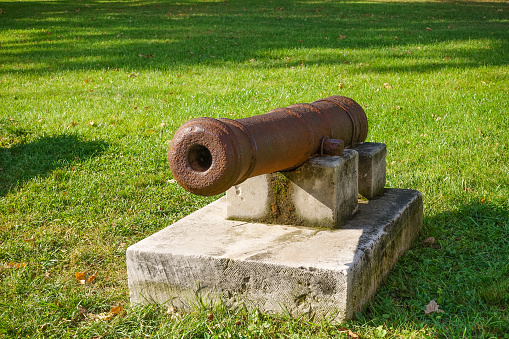 Old cast-iron gun standing on a stone plate on green grass