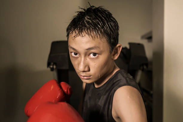 жесткие и прохладно молодой мальчик штамповки на тяжелый мешок . 13 или 14 лет азиатский подросток подготовки тайского бокса тренировки гляд� - 13 14 years стоковые фото и изображения