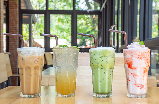 Iced Coffee, Honey Lemon Soda , iced green tea and strawberry smoothie in glass on the wooden table Background glass windows and  tree.