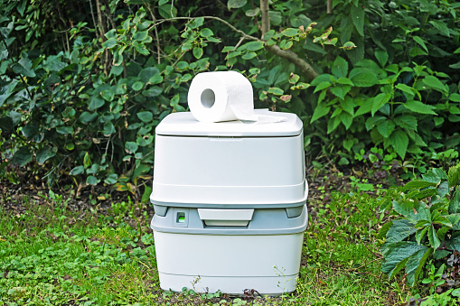 Chemical portable toilet and toilet paper roll. Single portable toilet standing on a green nature courtyard background