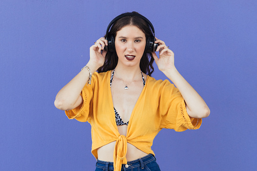 Cool Young Women Listening To Music Under Over-Ear Headphones Against Purple Wall