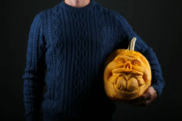 Photo of Man holding Jack-O-Lantern pumpking with creepy smile for all hallows eve. Halloween background.