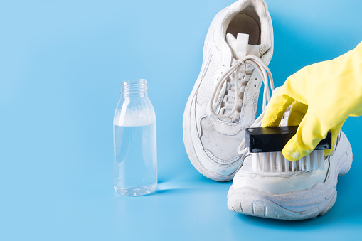 Dirty white sneakers with brush and special tool for cleaning them on blue background. Hand in protective gloves. protective gloves. Washing concept. Regular care about sneakers. Space for text.