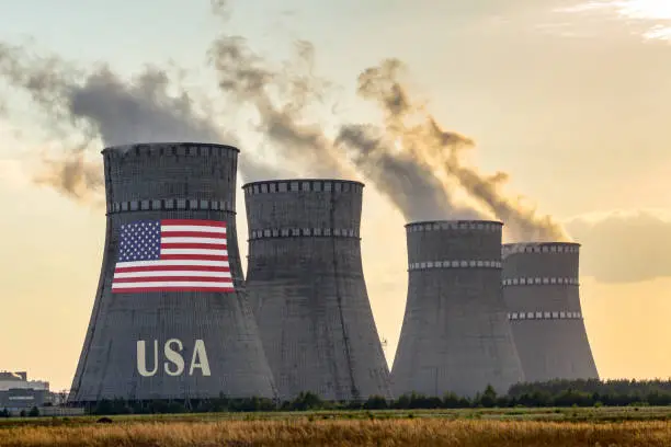 Photo of Nuclear plant chimneys displaying flag of USA or United States Of America with according text. Energy pollution accidents in a country concept.