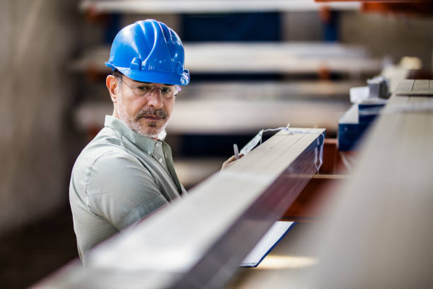 Mid adult manager making inspections in industrial building. Mid adult quality control inspector working on labels of manufactured products in a factory. metallurgy analysis stock pictures, royalty-free photos & images