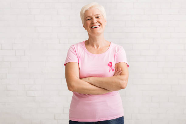 mujer mayor en rosa pecho cáncer camiseta de pie sobre la pared blanca - breast cancer fotografías e imágenes de stock