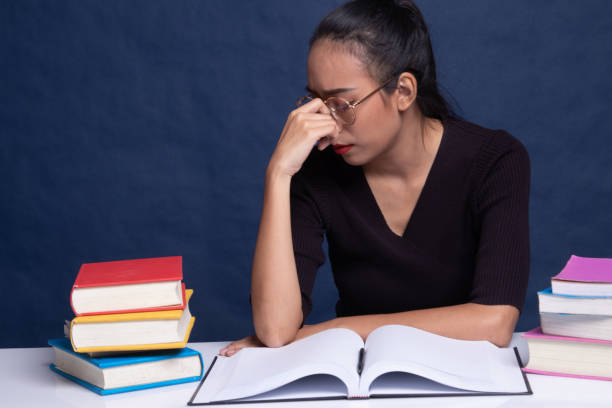 istock Exhausted Asian woman got headache read a book with books on table. 1178522982