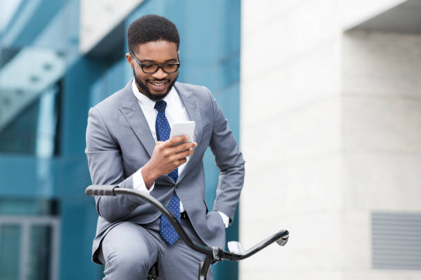 istock Happy afro businessman using smartphone, riding on bicycle 1178523675