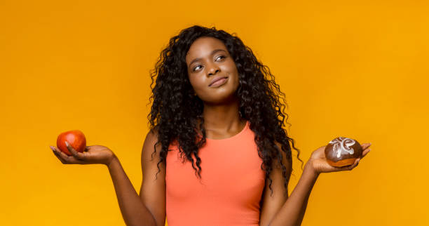 young woman making choice, donut or apple - cake pick imagens e fotografias de stock