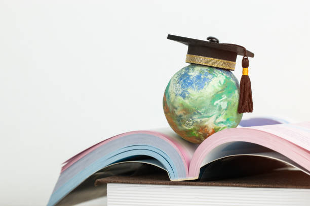 Study abroad education in Global ideas: Graduated cap on top global model on open textbook in library. Concept of studying international educational,reading book bring success degree in life
