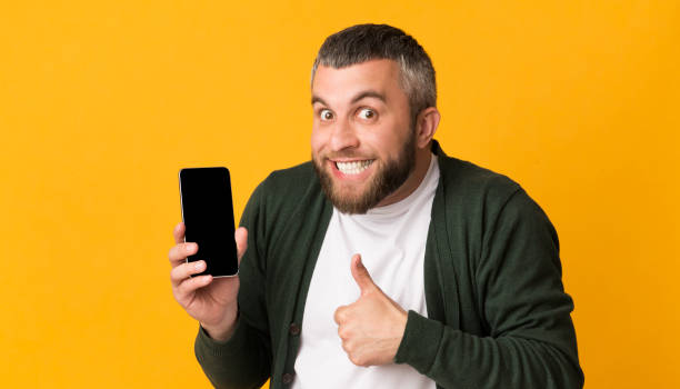 istock Playful bearded man holding smartphone, showing thumb up 1178527034