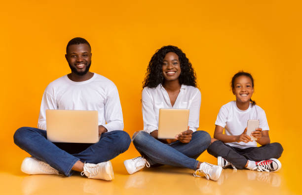 happy black family sitting with different gadgets in hands - couple laptop computer digital tablet imagens e fotografias de stock