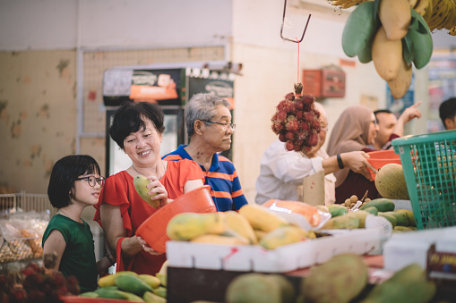 a group of asian customer in front of the fruit stall selecting and choosing fruits during weekend with their family members