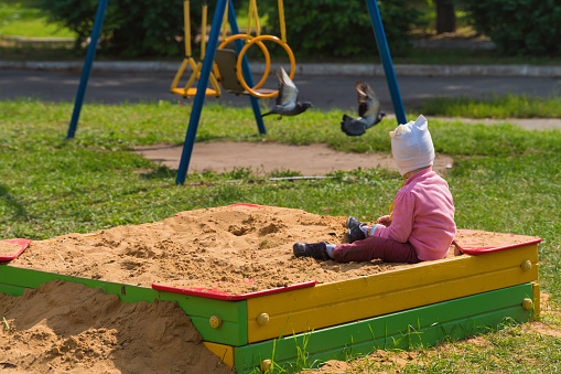 child sitting in a sandbox and looks at birds flying