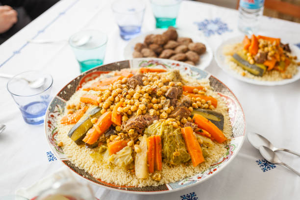 Couscous traditional moroccan food family gathering Traditional Moroccan homemade Couscous plate on a white clothed table served with out of focus kefta, with glasses, spoons, water and smaller plate . Morocco family gathering concept. hari raya family stock pictures, royalty-free photos & images