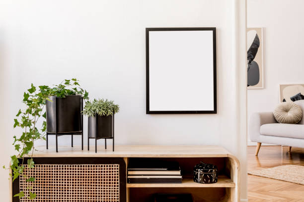 istock Modern scandinavian home interior with mock up photo frame, design wooden commode, plants in black pots, gray sofa, books and personal accessories. Stylish home decor. Template. Ready to use. 1178533276