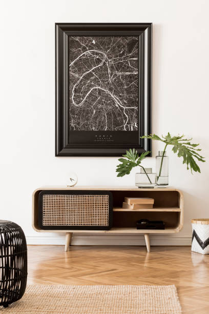 istock Modern scandinavian living room interior with black mock up poster map frame, design commode, tropical leaf in vase, black rattan pouf, books and elegant accessories. Template. Stylish home decor. 1178533895