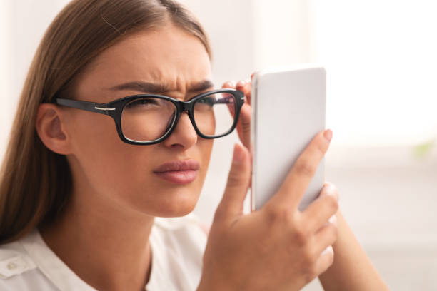 Girl Looking At Cellphone Through Eyeglasses Having Vision Problem Indoor Poor Eyesight Concept. Girl Looking At Cellphone Screen Through Eyeglasses Having Vision Problem Indoor. Selective Focus squint eyes stock pictures, royalty-free photos & images